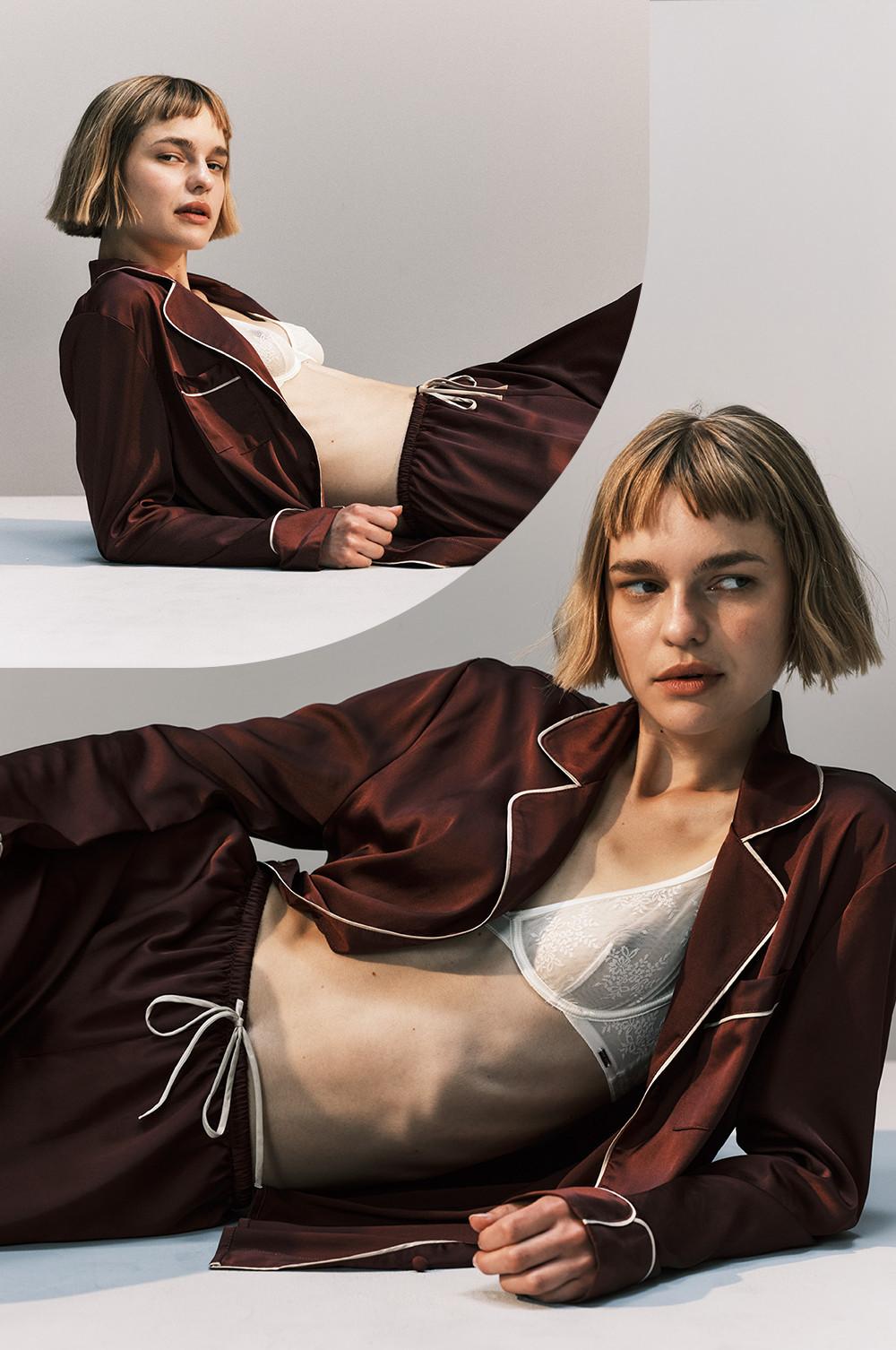 Model wearing burgundy pajama set with white piping and lace bralette underneath. Short bob haircut.