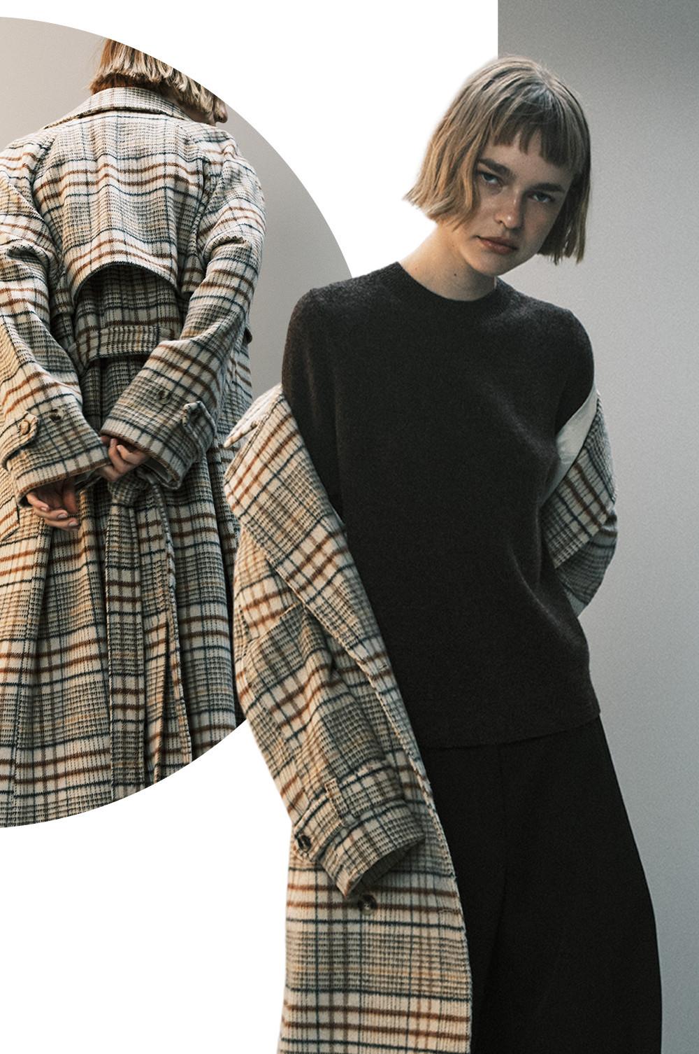Model wearing black outfit with plaid overcoat, displaying contrast between dark sweater and patterned coat.