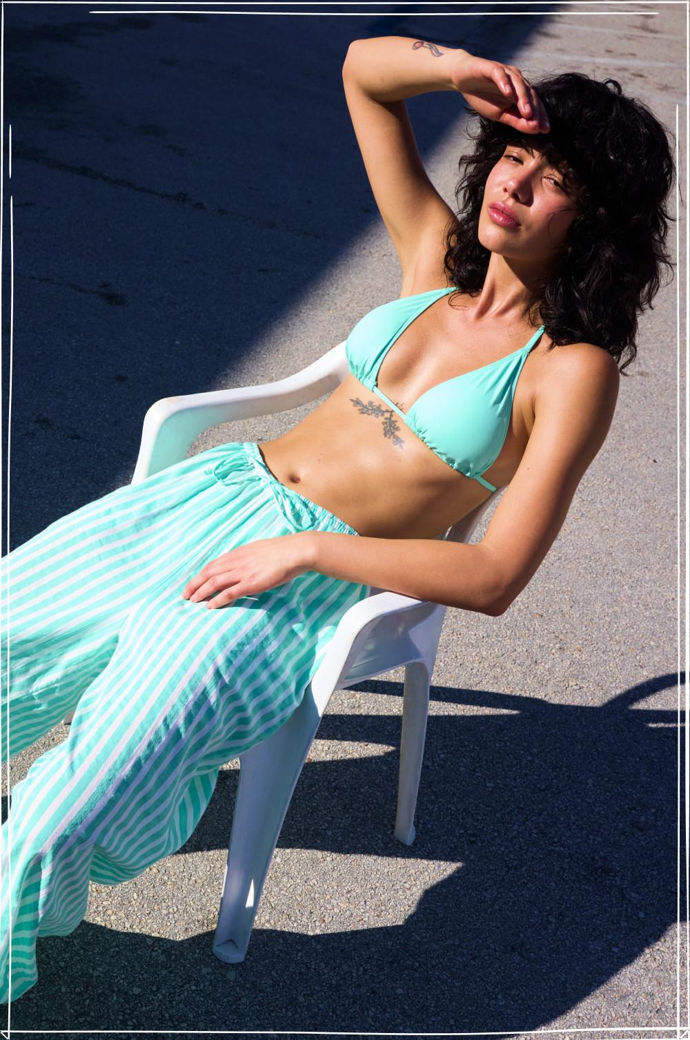Model relaxing in mint green striped bikini and matching sarong on poolside lounger.