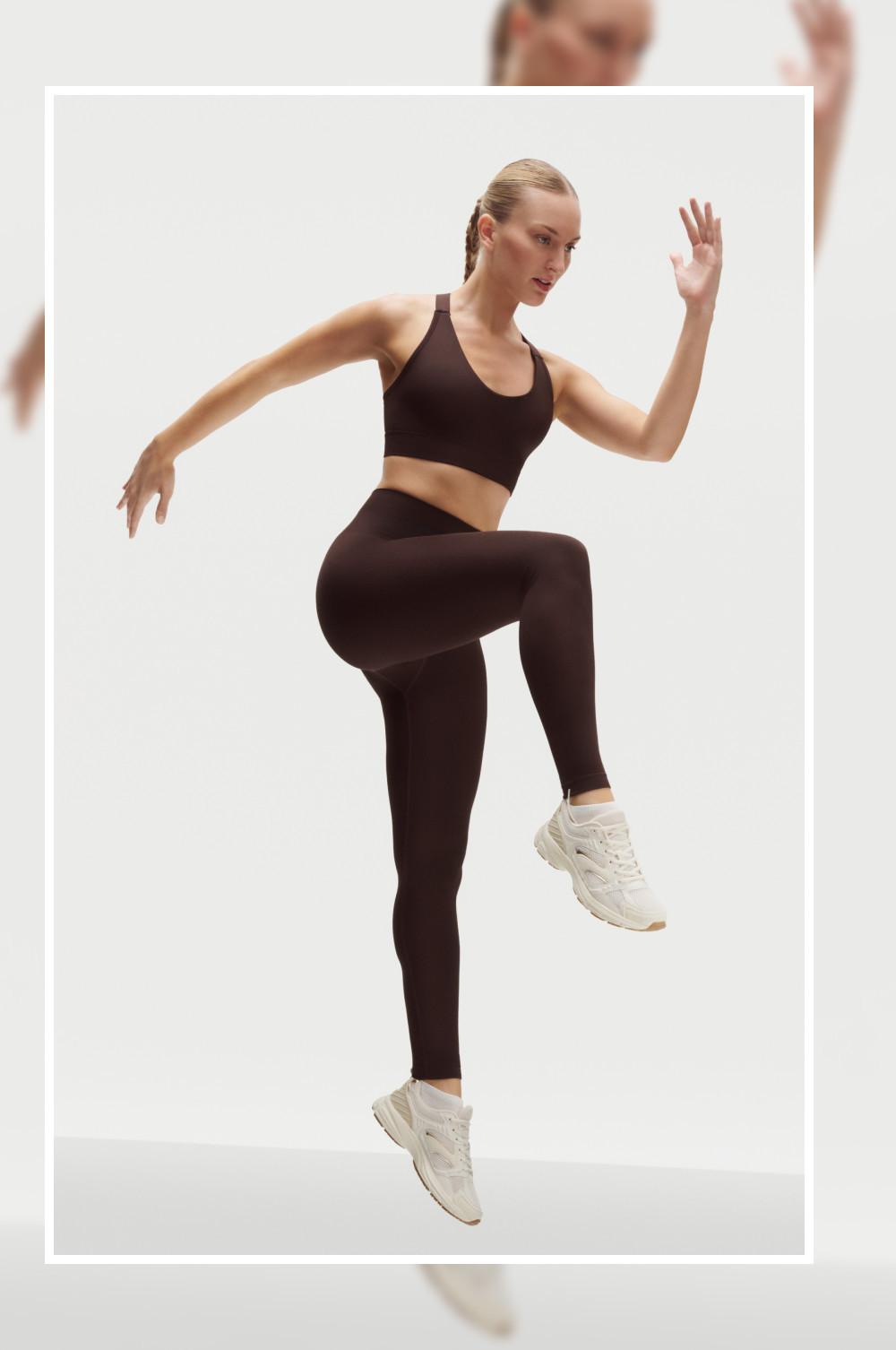 Modella che esegue un esercizio di sollevamento delle ginocchia indossando un reggiseno sportivo nero, leggings neri e scarpe da ginnastica bianche.