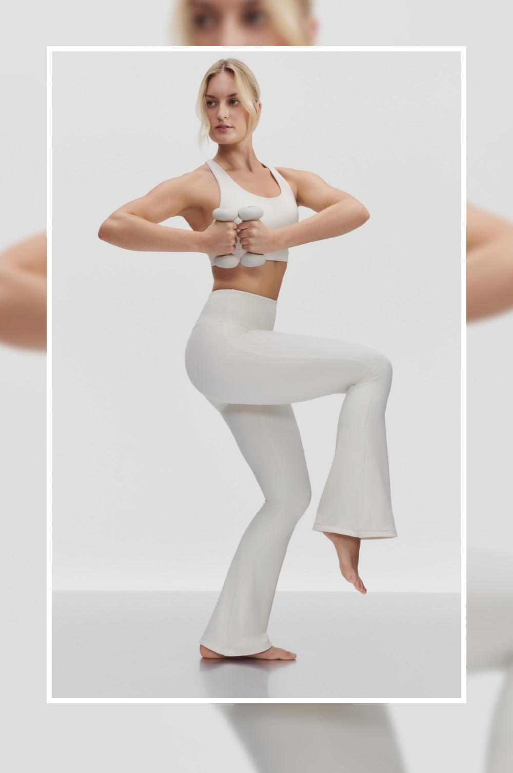 Modella che esegue uno squat indossando un reggiseno sportivo bianco e leggings svasati abbinati.