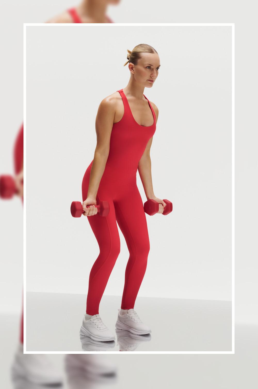 Modella in abbigliamento sportivo rosso che tiene in mano dei manubri mentre esegue un esercizio di potenziamento muscolare.