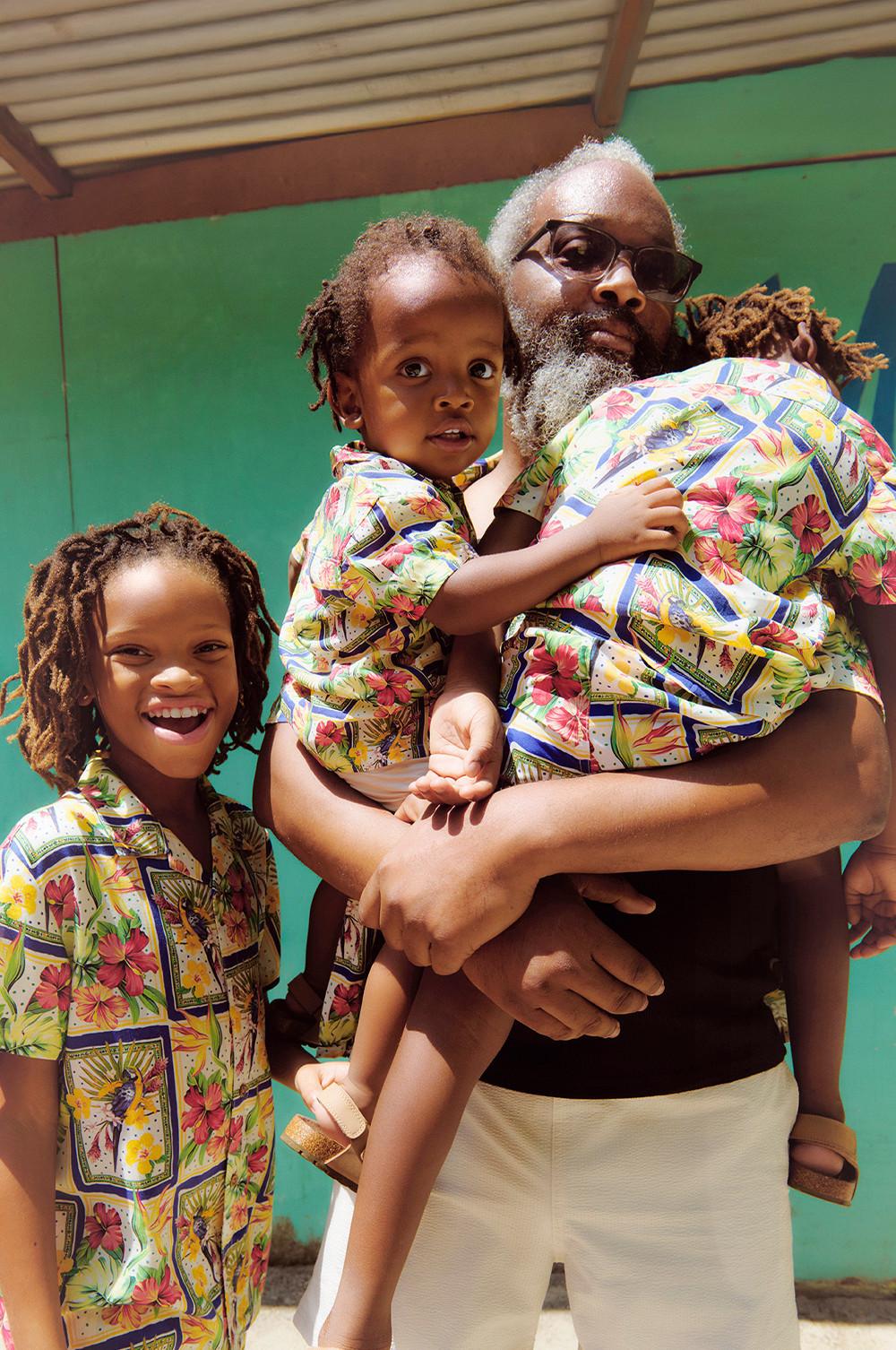 Family wearing matching vibrant floral print shirts against a green background.