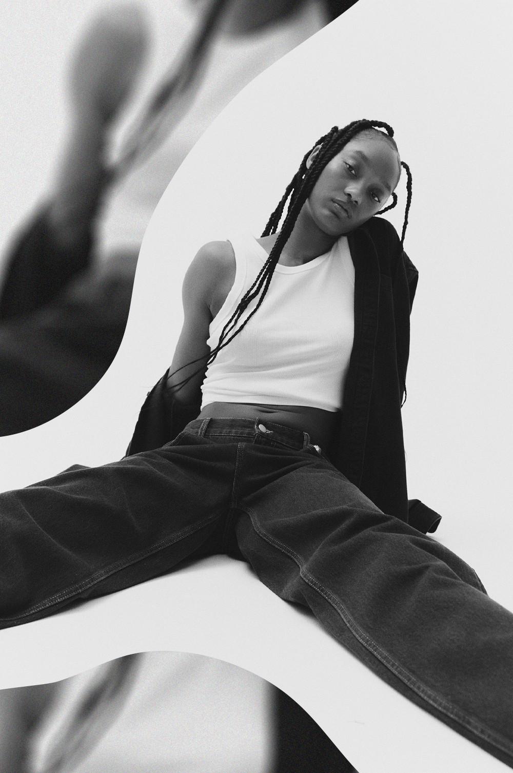 Model wearing white ribbed tank top with dark wide-leg pants and black cardigan draped over shoulder.