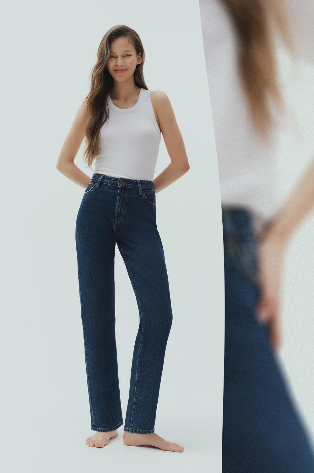 Model wearing white sleeveless tank top and dark blue high-waisted straight leg jeans.