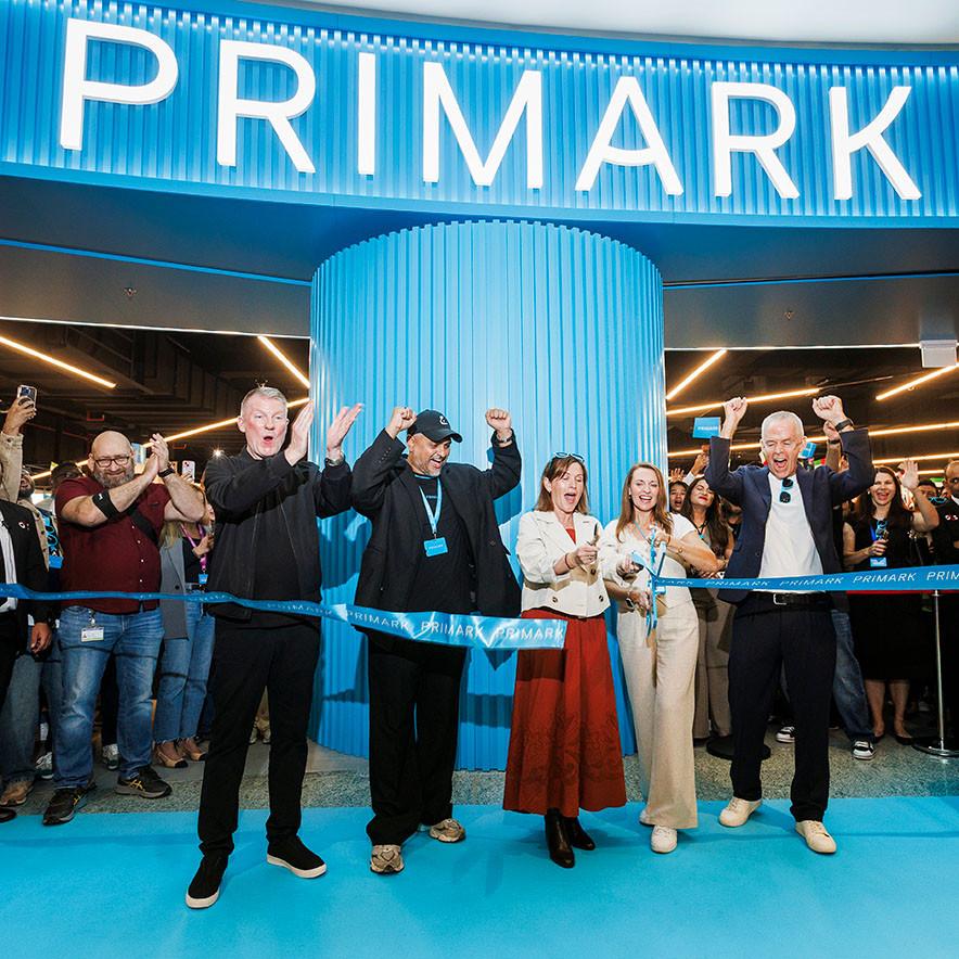 A group of people celebrating at a Primark store opening. They are cutting a blue ribbon.