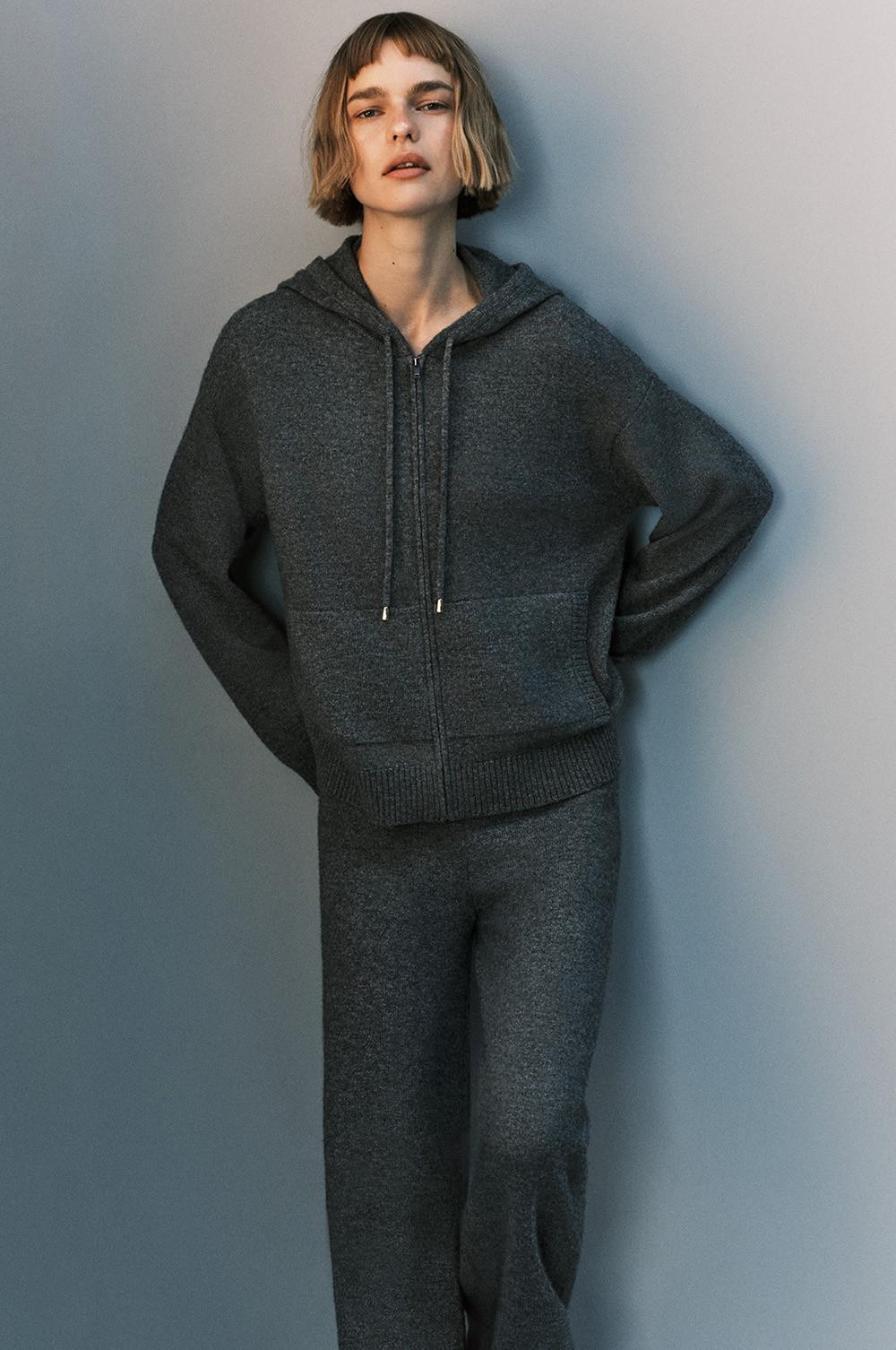 Person wearing a dark grey zip-up hoodie with matching loungewear trousers against a plain background.