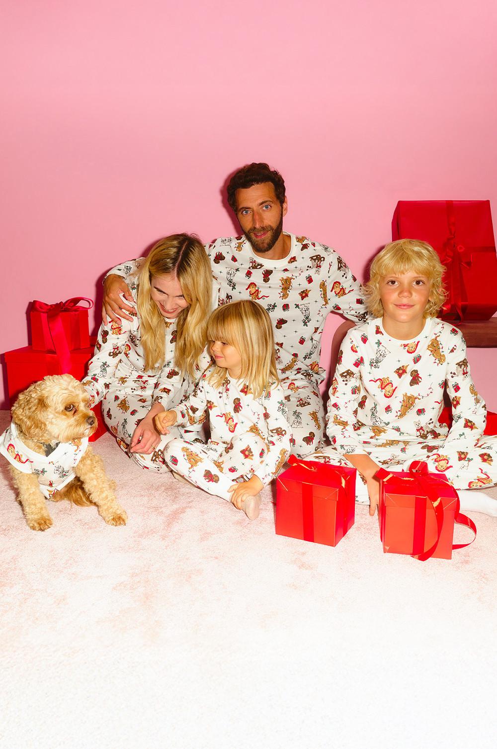 Family wearing matching animal print pyjamas with their dog, surrounded by red gift boxes.