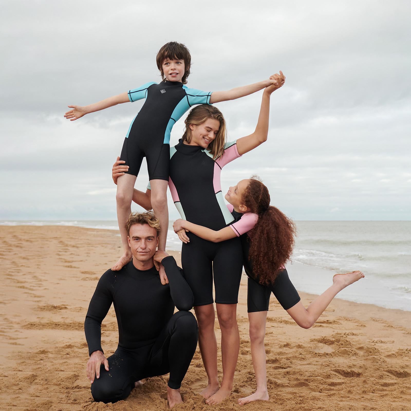 Famille portant des combinaisons de surf noires à coupe longue avec manches roses et bleues.