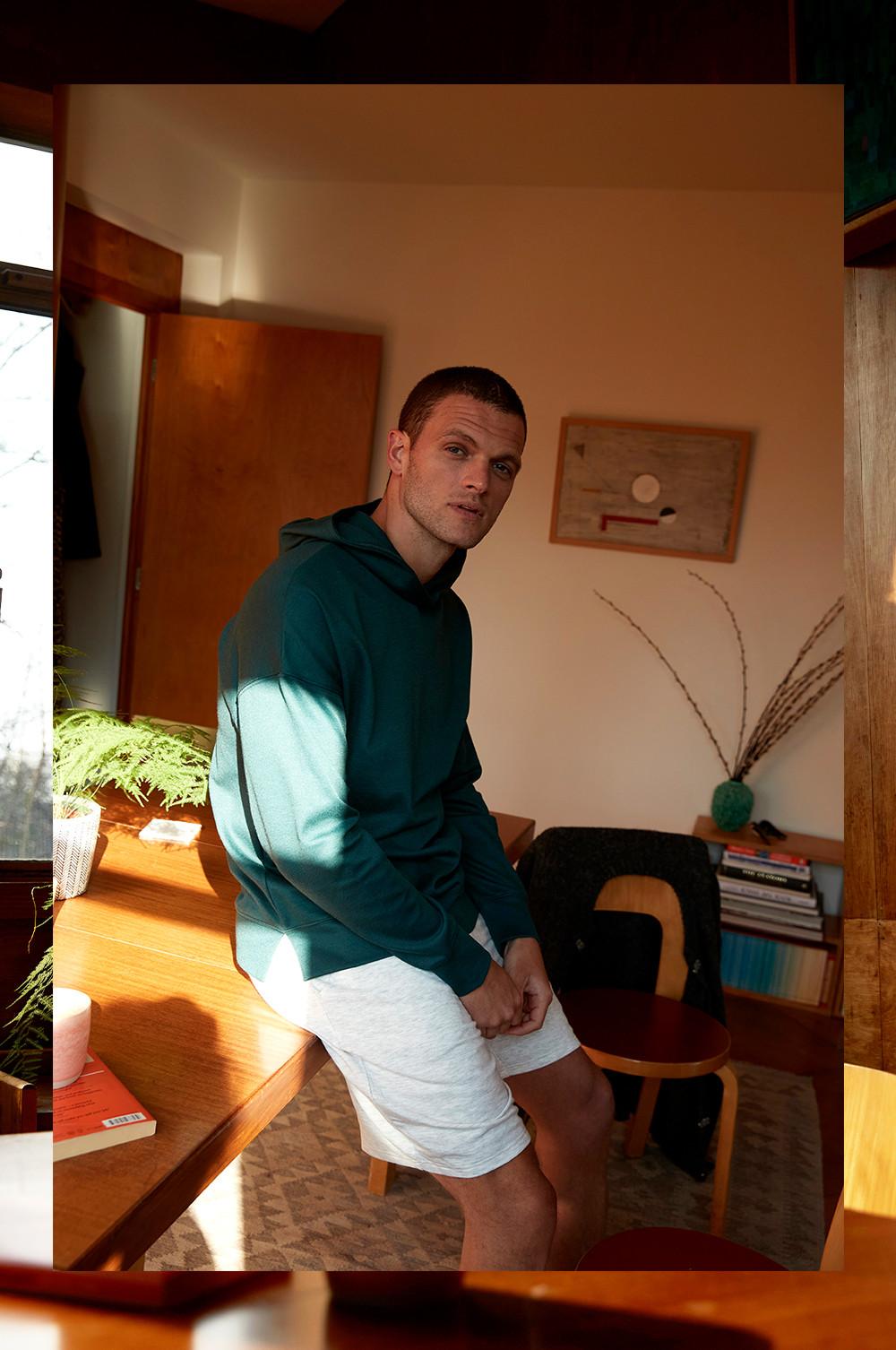 Model in grünem Kapuzenpullover und grauen Shorts