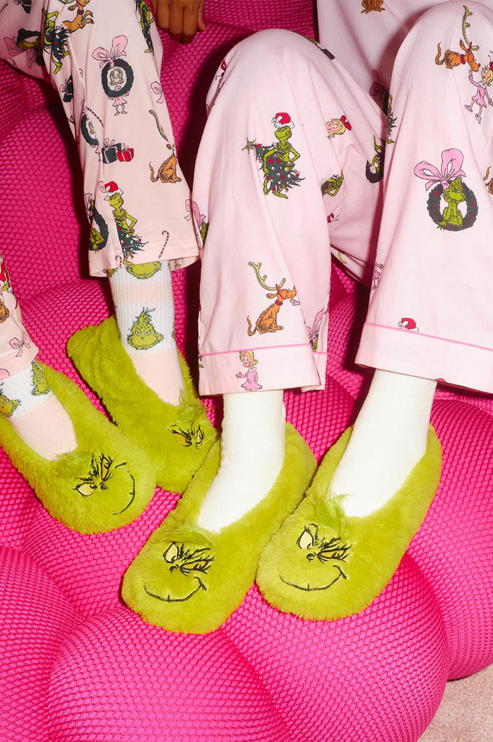 Pink Grinch-themed pyjamas with green fuzzy slippers featuring the Grinch's face on a bright pink surface.
