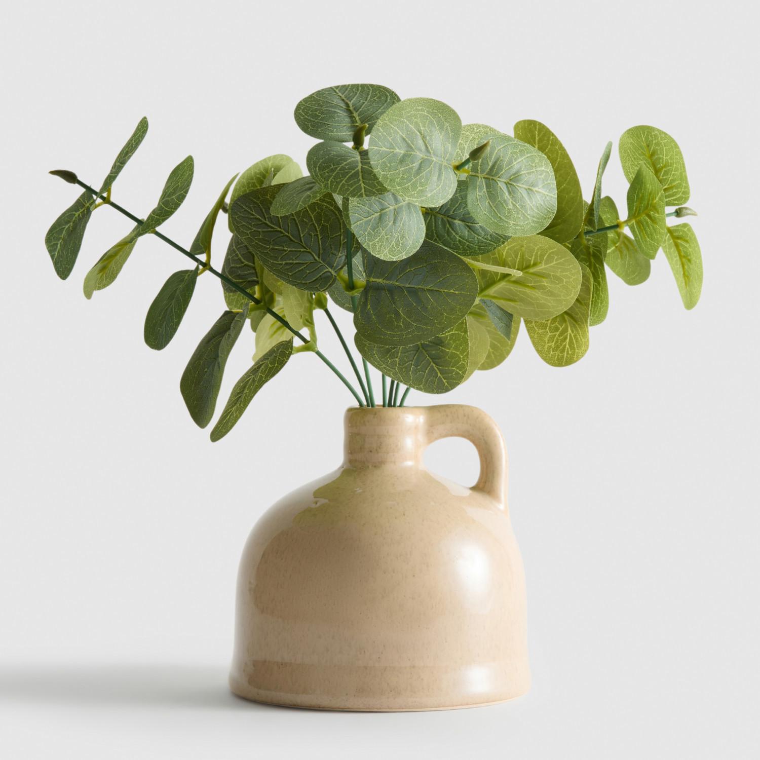 Artificial eucalyptus stems with round green leaves displayed in a beige ceramic jug with handle.