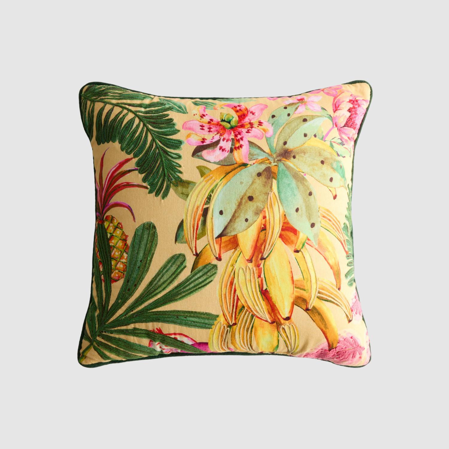 Decorative cushion with tropical print featuring palm leaves, pink flowers, and yellow foliage on beige fabric.