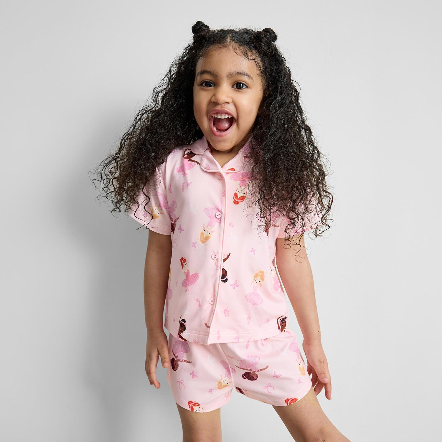 Young girl wearing pink short-sleeved pyjamas with princess print, smiling joyfully.