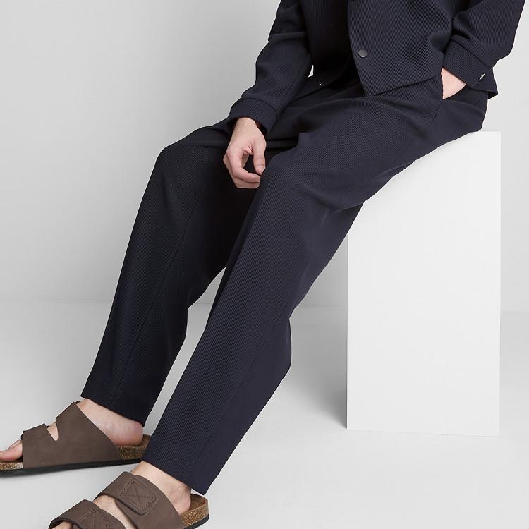 Person sitting wearing navy pinstripe suit trousers with brown leather sandals.