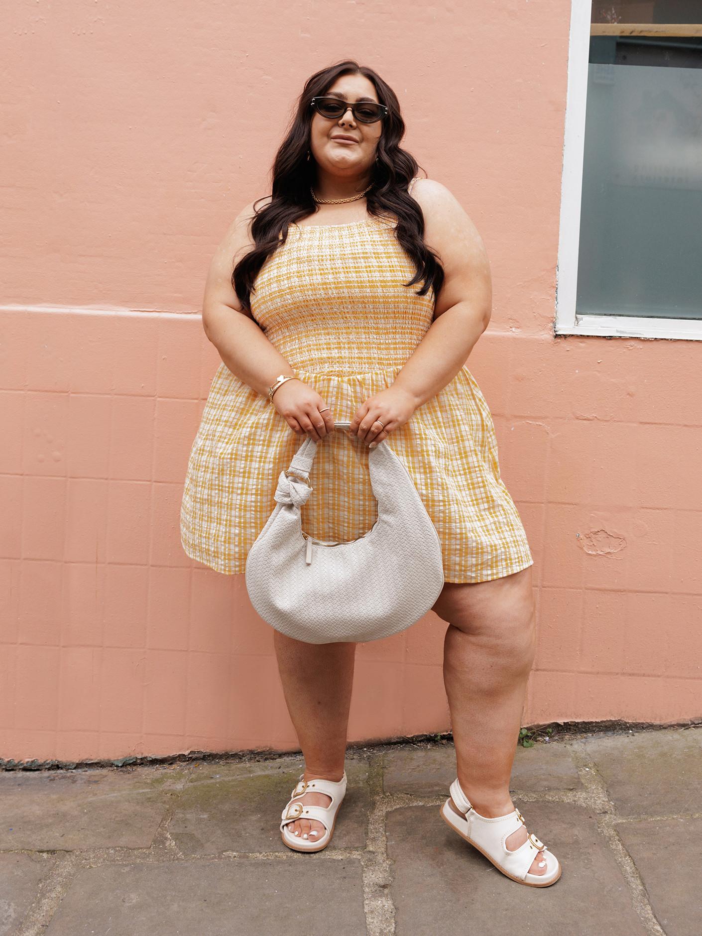 Modelo con un vestido corto amarillo, fruncido y con tirantes, un bolso de polipiel blanco y sandalias con dos tiras.