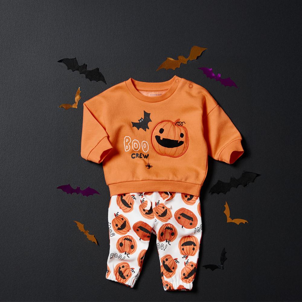 Orange Halloween baby outfit with "BOO CREW" and pumpkin design on sweatshirt, matching pumpkin print pants, surrounded by decorative bats.
