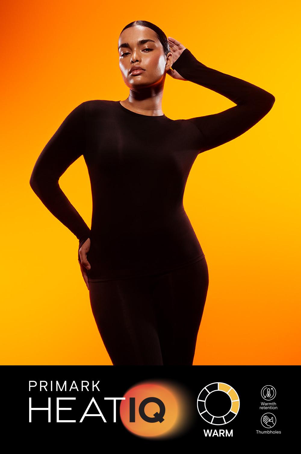 Person wearing black Primark HEATIQ bodysuit against orange background, showcasing warmth retention features.