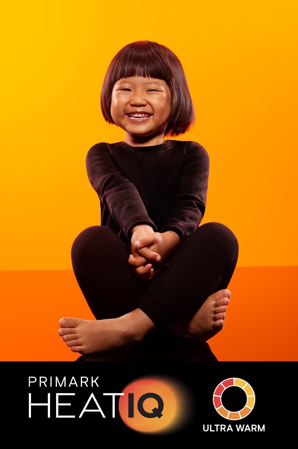Child wearing black Primark HEATIQ thermal clothing against orange background. Ultra warm collection.