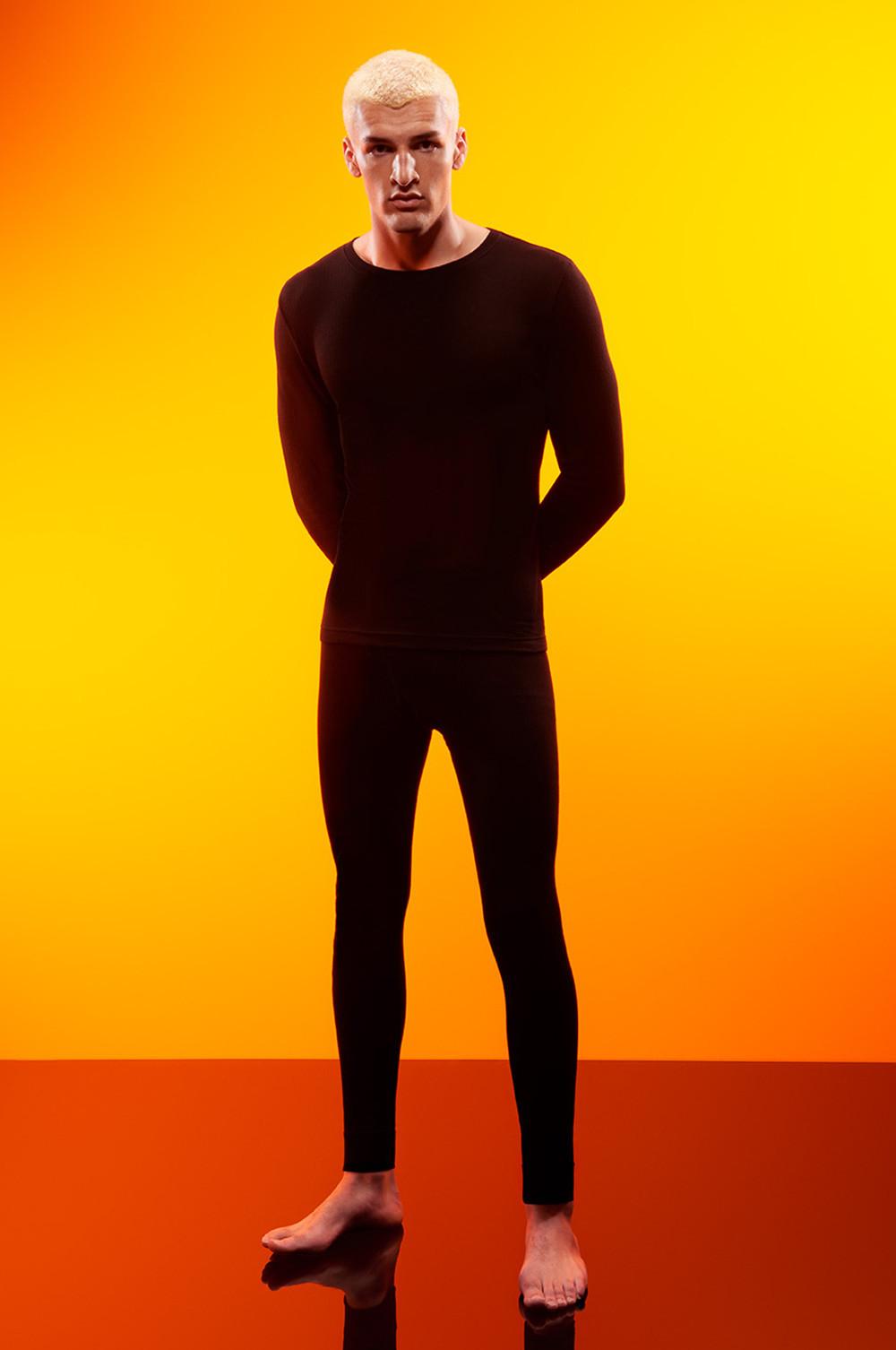 Person wearing black fitted long-sleeve top and leggings against vibrant orange background.