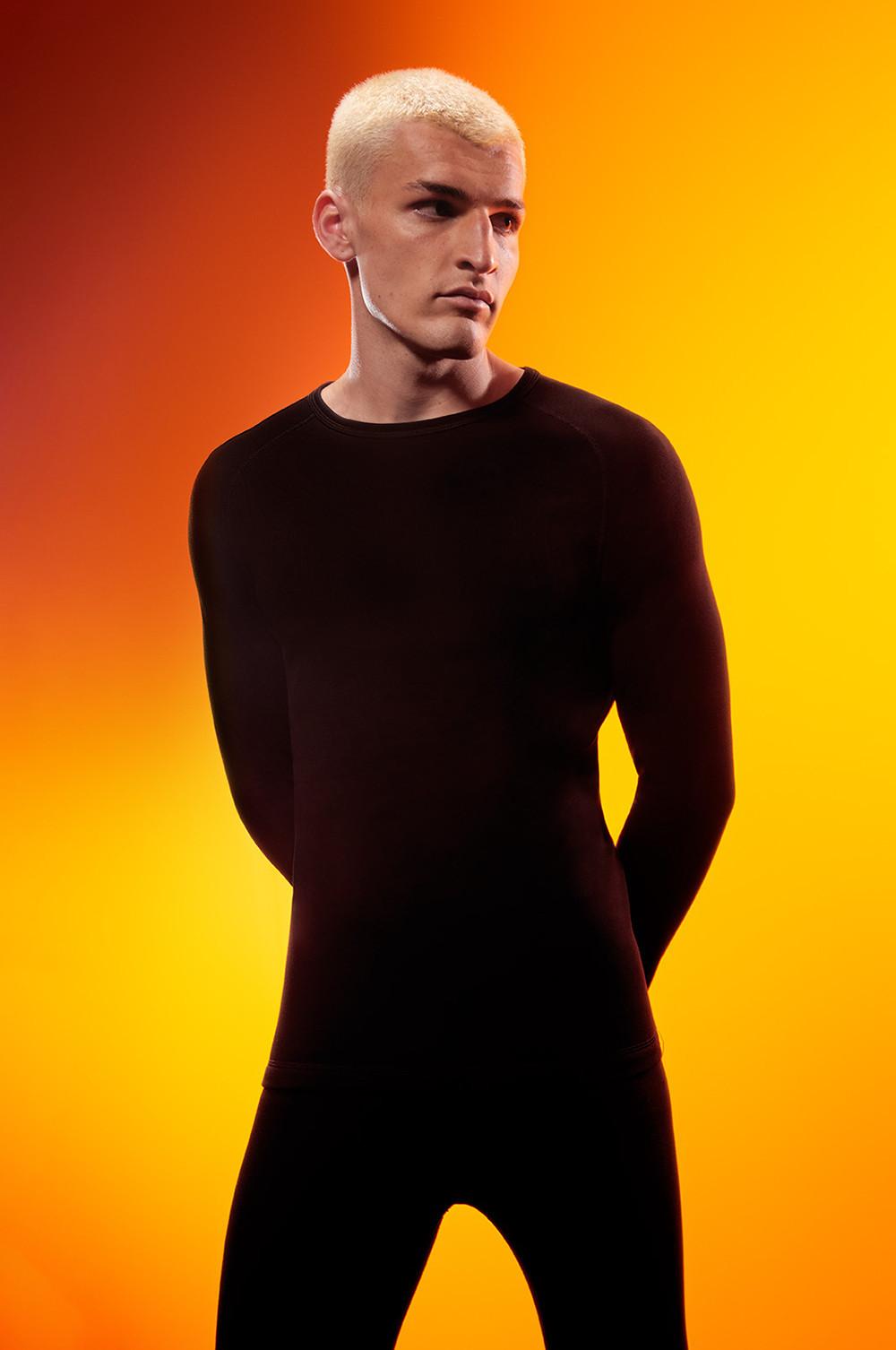 Person wearing black fitted long-sleeve athletic top against vibrant orange-yellow gradient background.