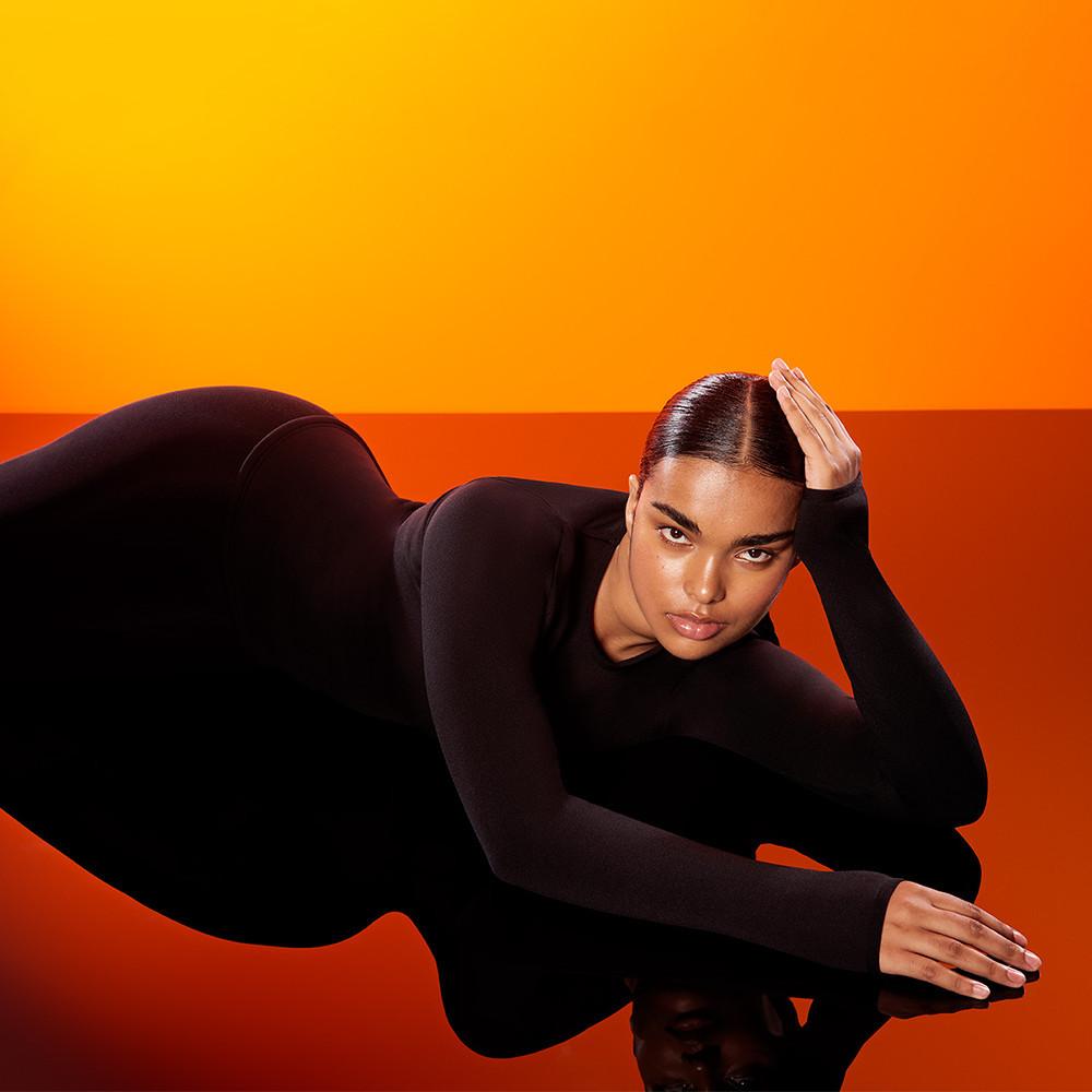 Person wearing a fitted black bodysuit posing against a vibrant orange gradient background.
