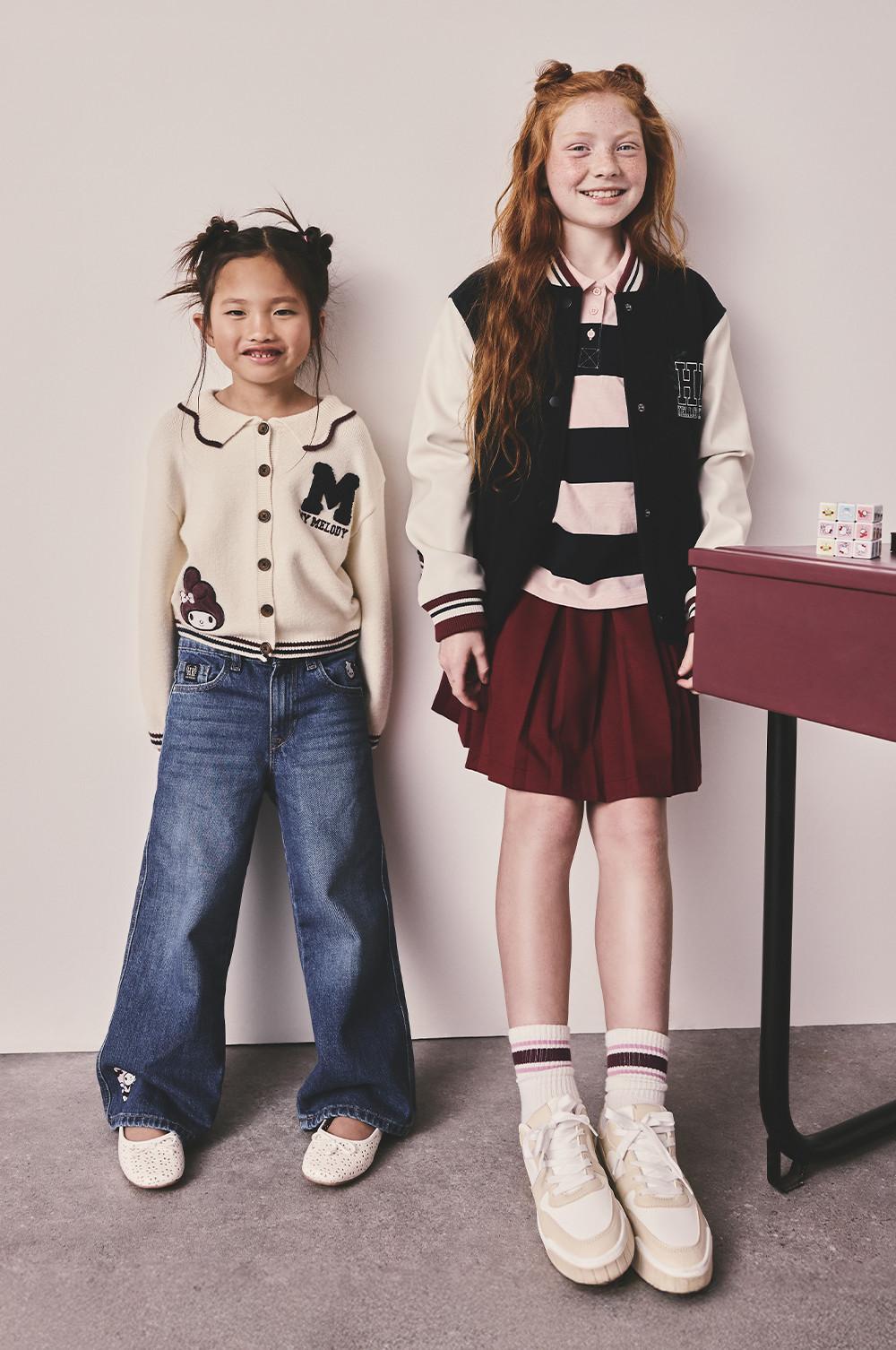 Due bambine indossano giacche in stile college: una panna con il logo di una M e l'altra una giacca bianca e nera e gonna bordeaux.