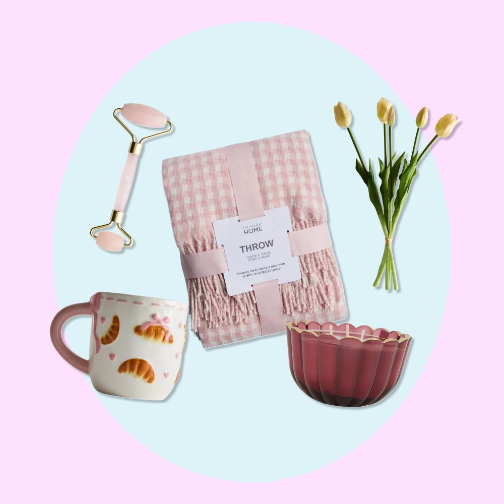 Pink home accessories including a throw blanket, facial roller, croissant mug, decorative bowl and yellow tulips.