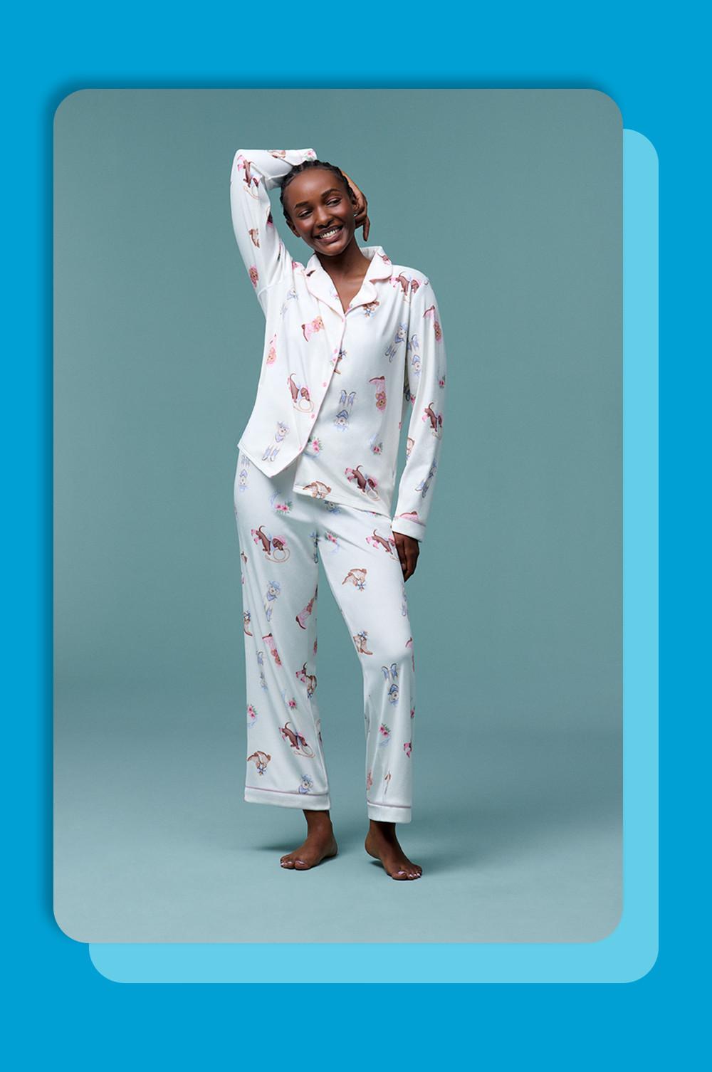Lachend model draagt een witte pyjama met dierenprint bestaand uit een jasje met reverskraag en een broek.