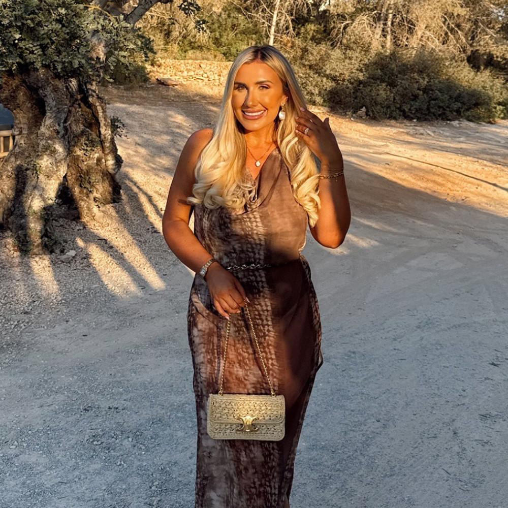 Brown patterned maxi dress with gold-toned chain handbag in a sunny outdoor setting.