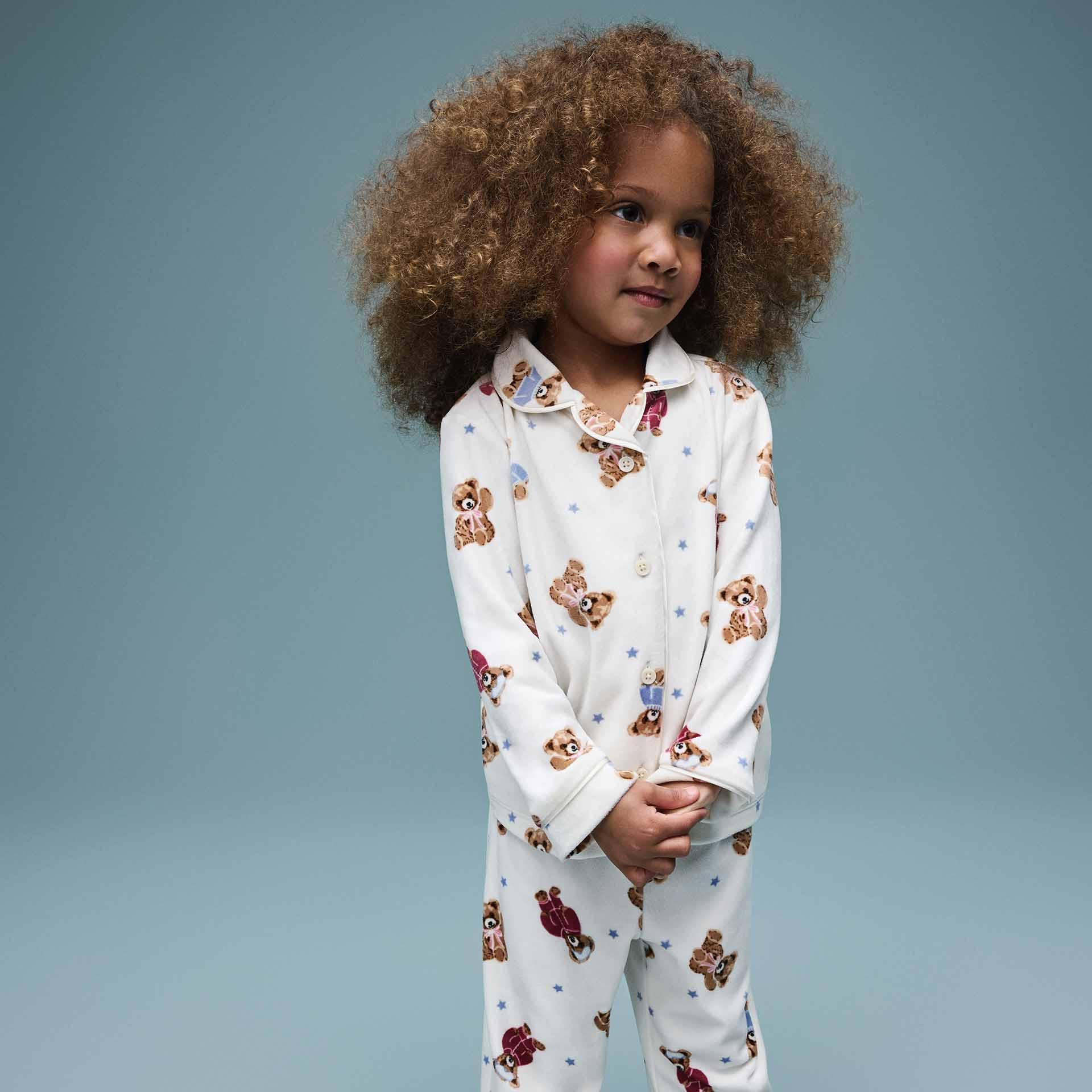 A young girl with curly hair wearing white pjs featuring a pattern of teddy bears and blue stars.