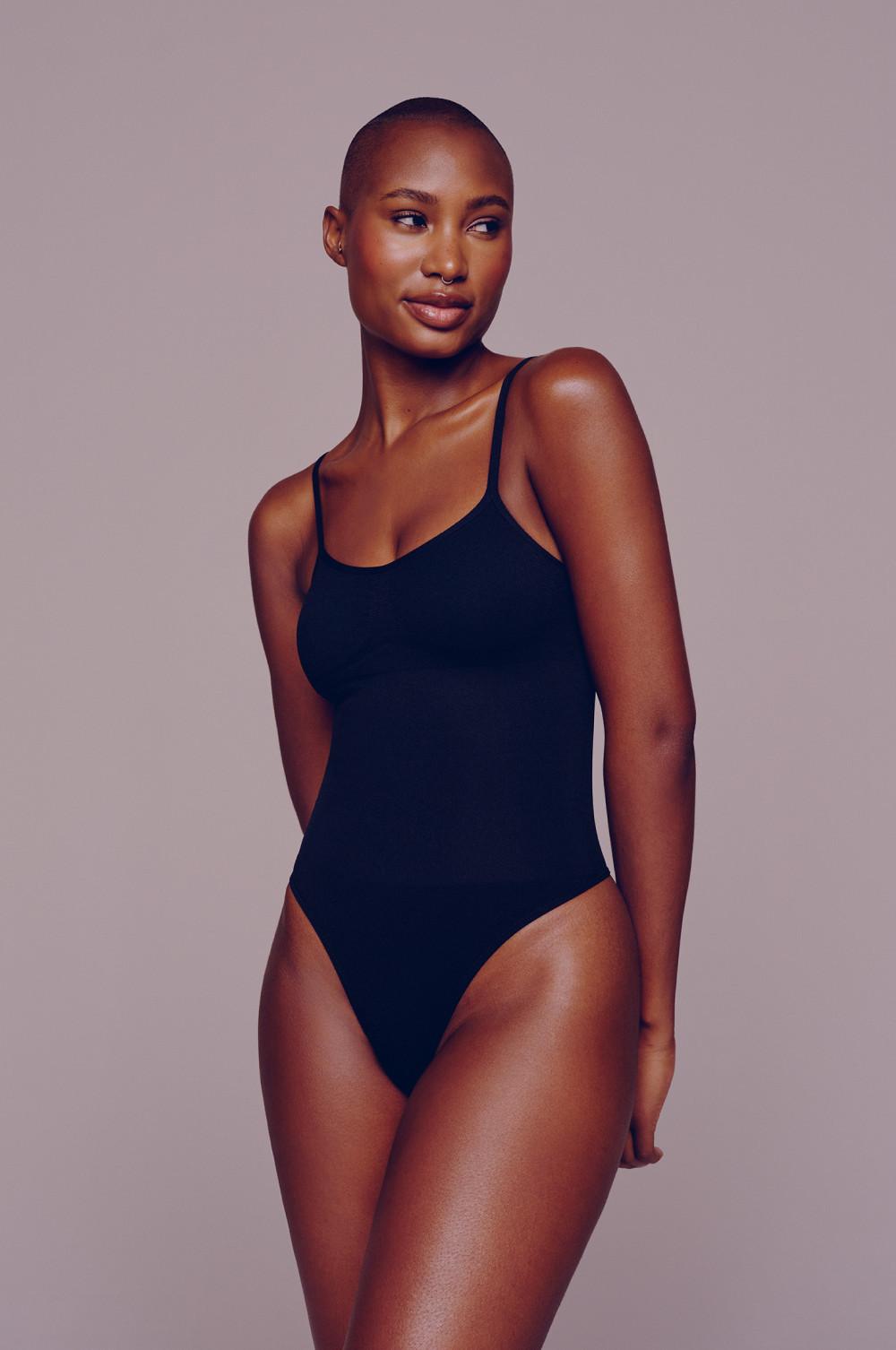 Model wearing a black scoop neck bodysuit with thin straps and high-cut leg design.