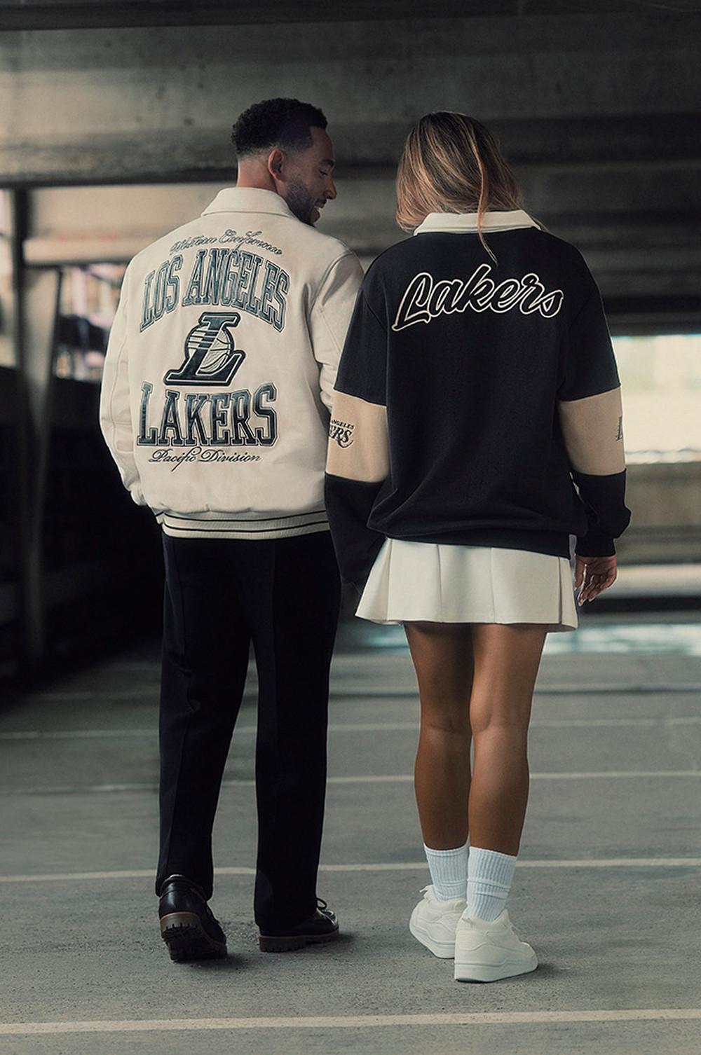 Pareja paseando junta con chaquetas de Los Angeles Lakers a juego, una de color crema y otra negra.