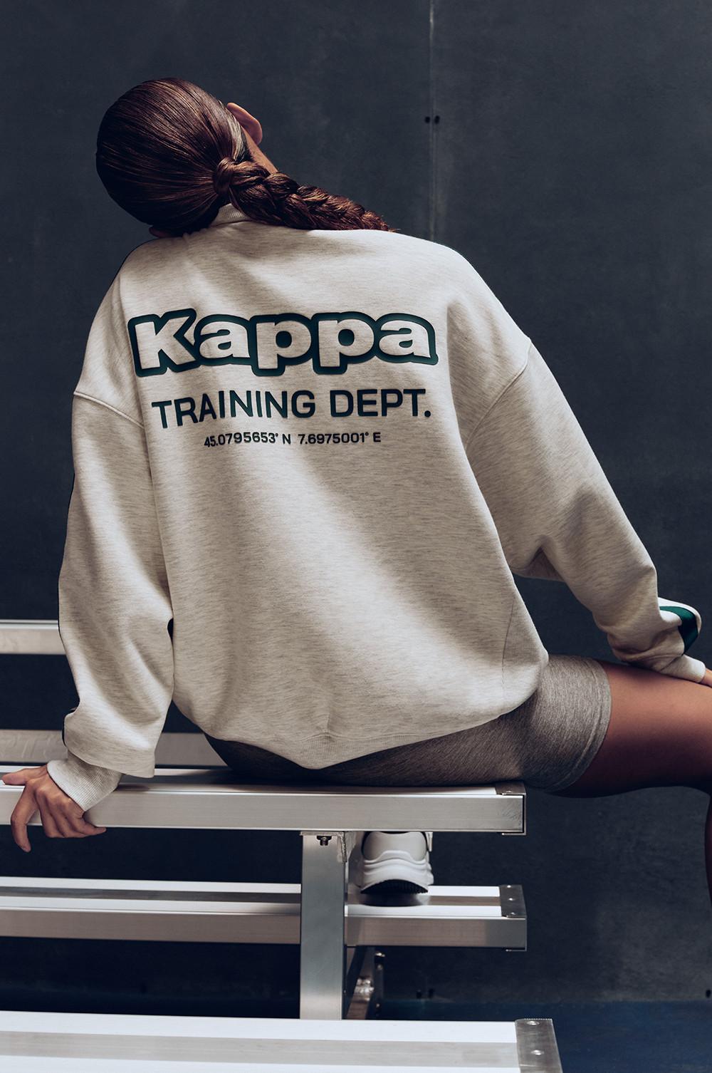 Persona che indossa una felpa beige Kappa Training Dept seduta su una panchina bianca.