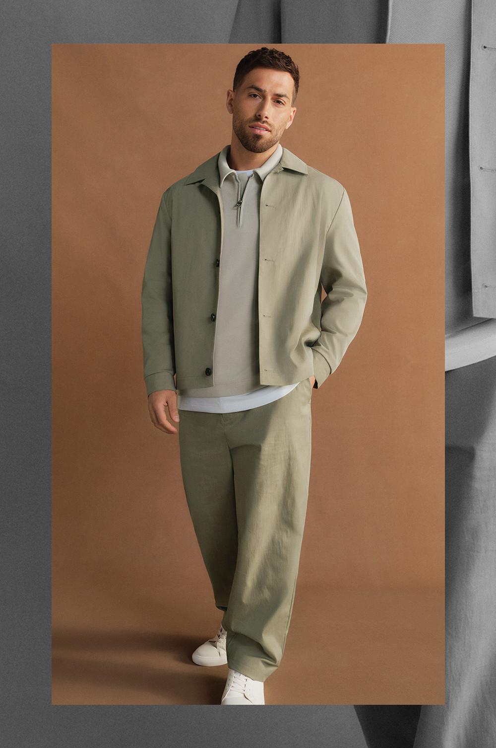 Personne portant un look vert sauge composé d'une veste, d'un haut à col zippé et d'un pantalon, avec des baskets blanches aux pieds.