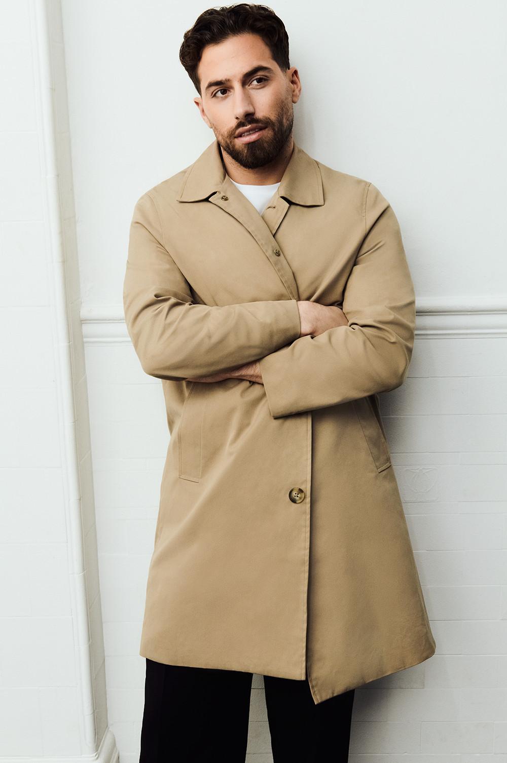 Kem wearing a beige mac, white t-shirt, black trousers and under jacket