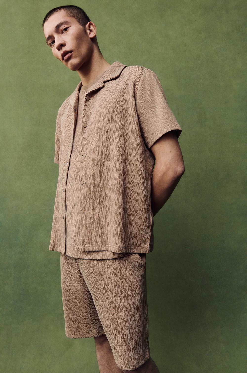 Textured tan short-sleeve shirt and shorts set with button-front styling against a green backdrop.