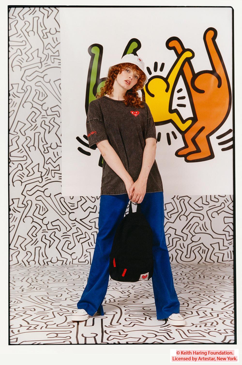 Modella che indossa maglia grigia, cappello alla pescatora e zaino Keith Haring