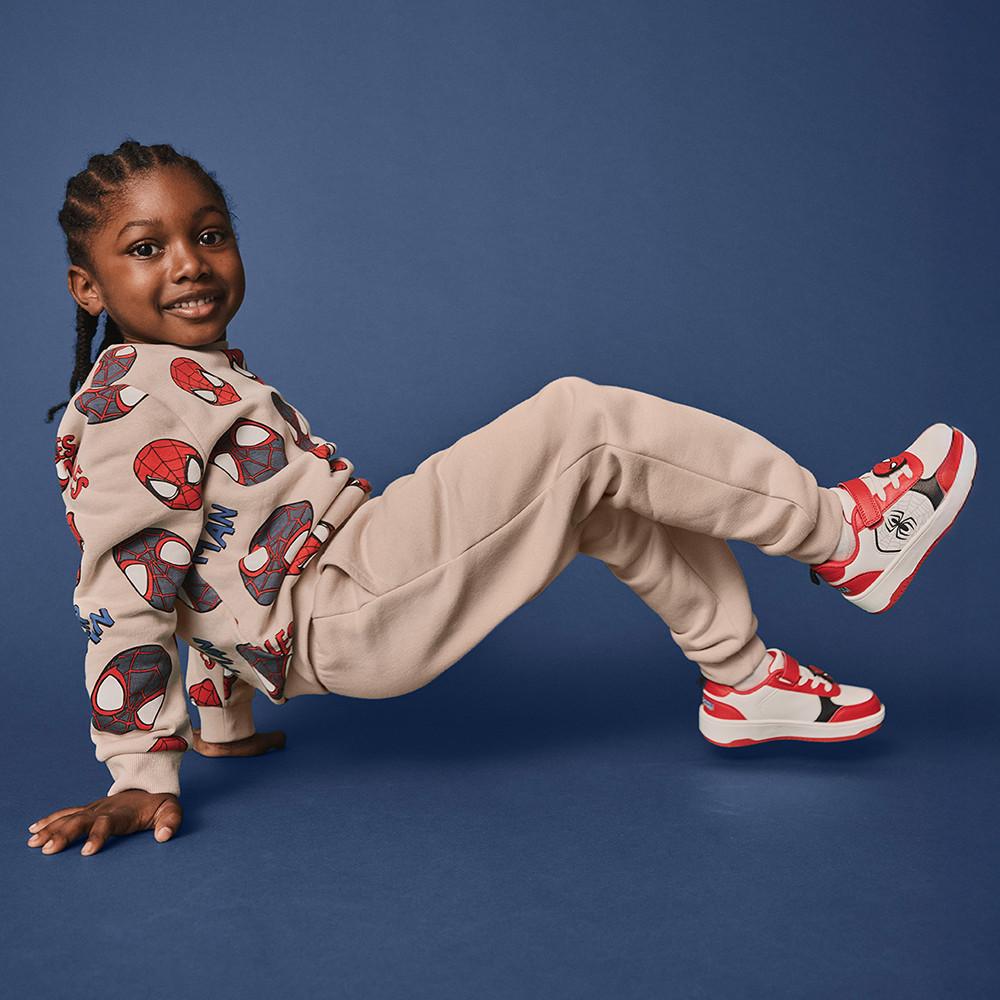 Bambino che indossa una felpa di Spiderman, scarpe da ginnastica e pantaloni da tuta beige
