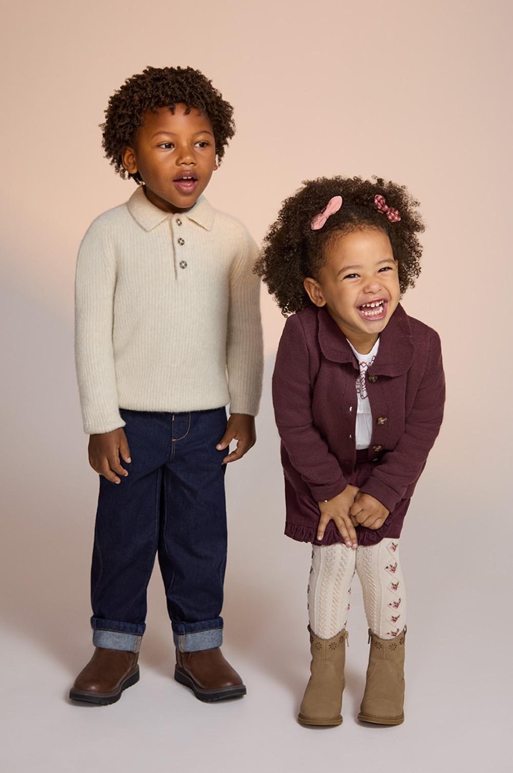 Two children wearing autumn outfits - cream polo jumper with jeans and burgundy cardigan with patterned tights and boots.