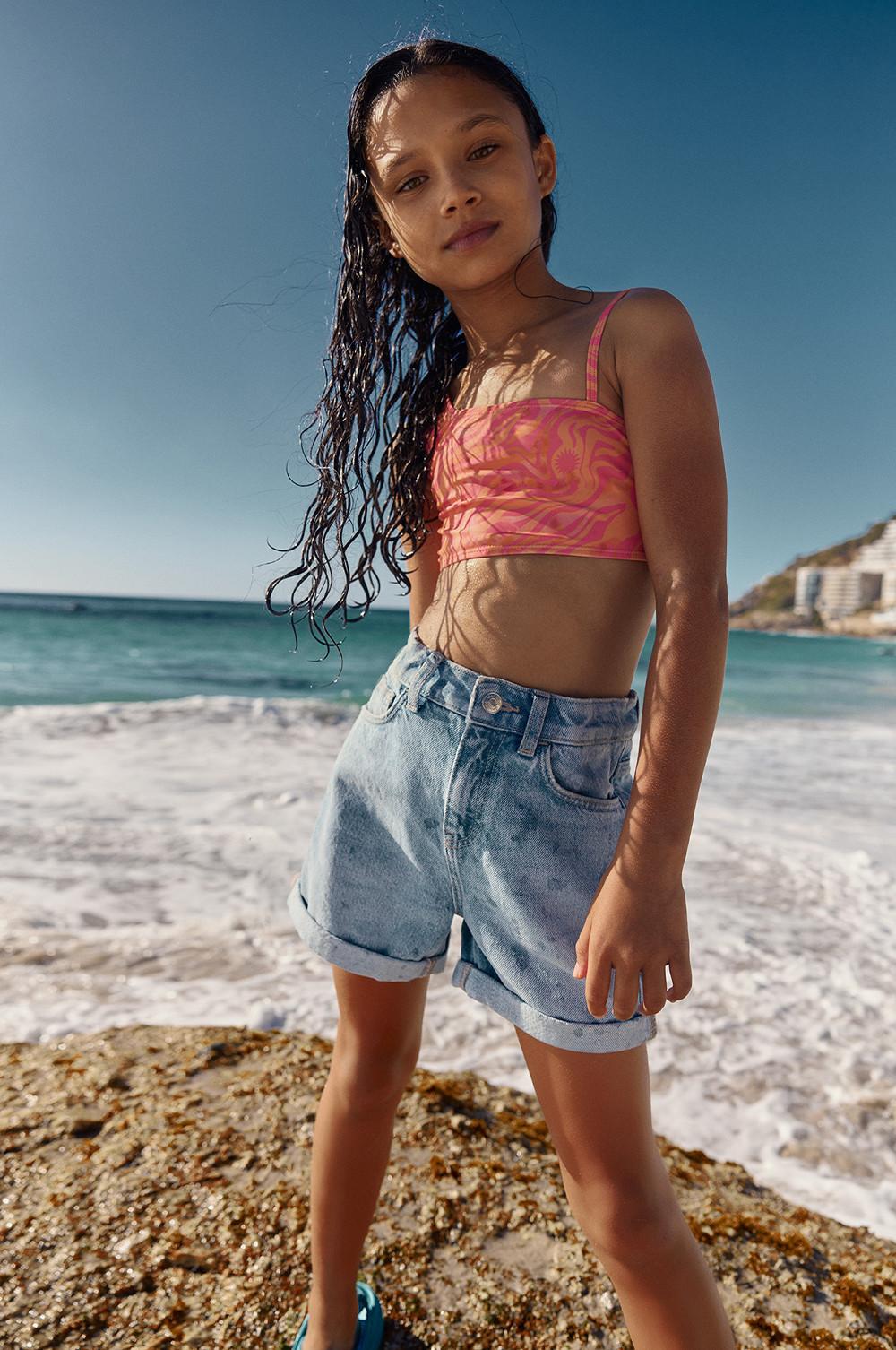 Bambina che indossa un top bikini corallo e shorts in denim