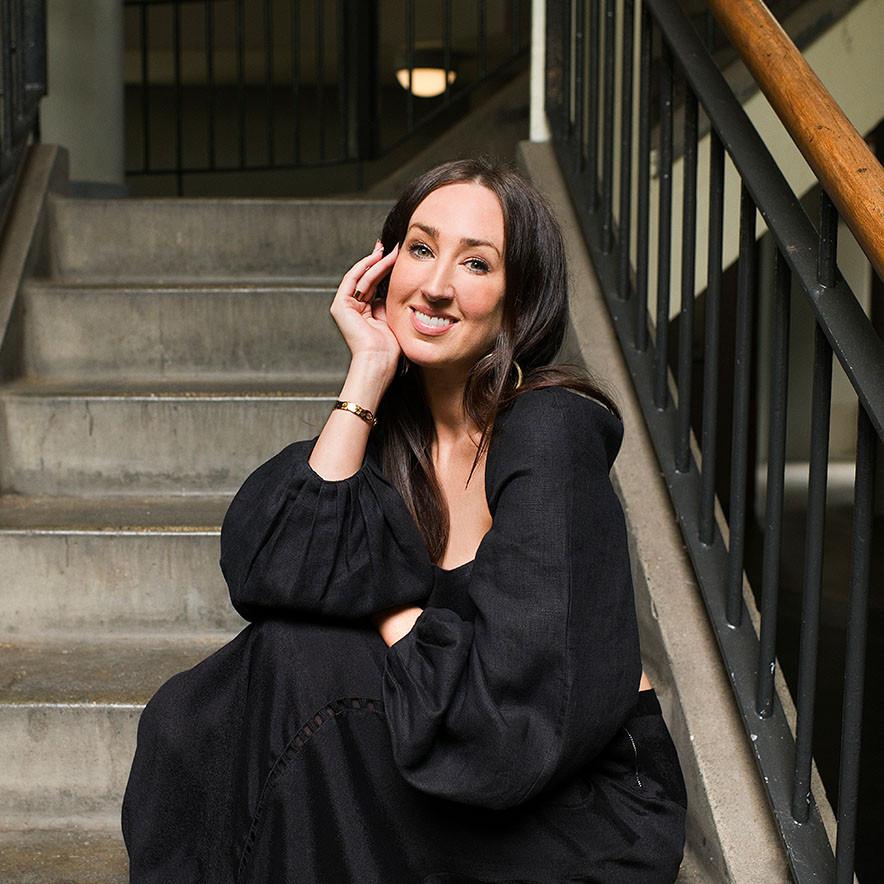Best selling author and clothing care expert Laura De Barra, sitting and smiling in a black dress.