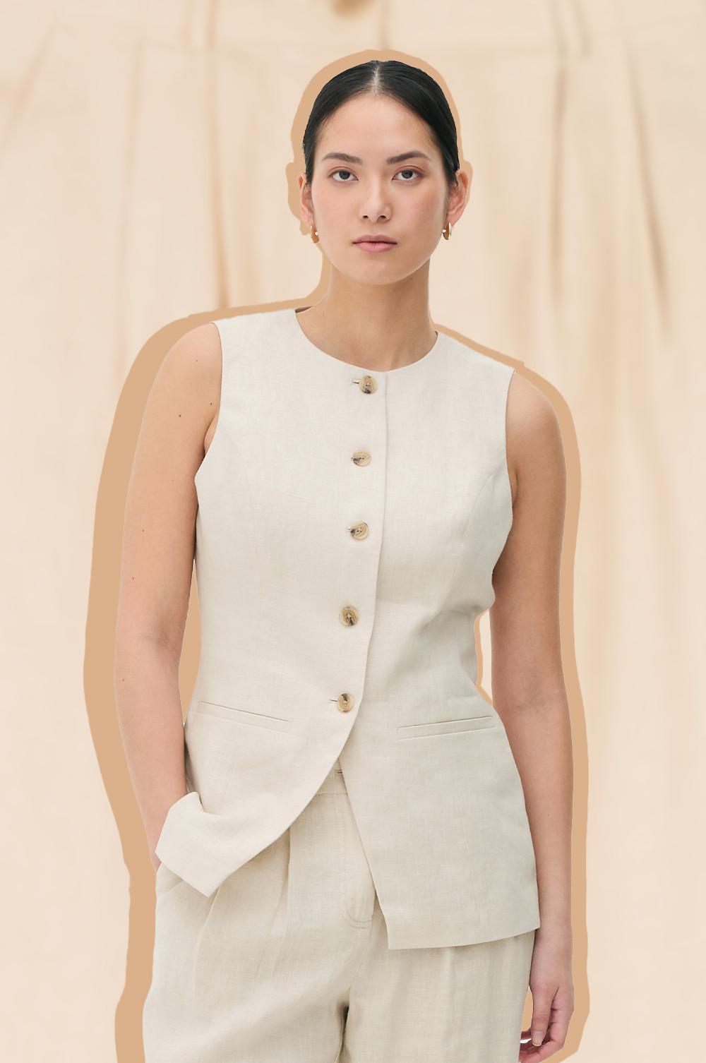 Sleeveless beige waistcoat with buttons, worn over matching trousers. Hands in pockets.