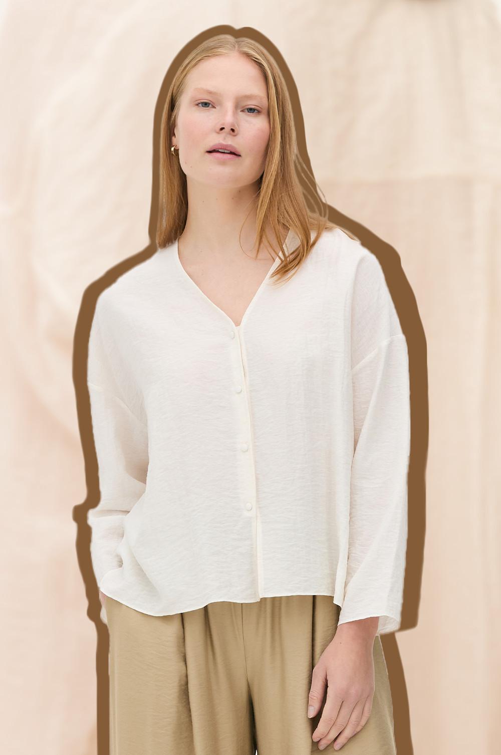 White button-up blouse with long sleeves paired with beige trousers.
