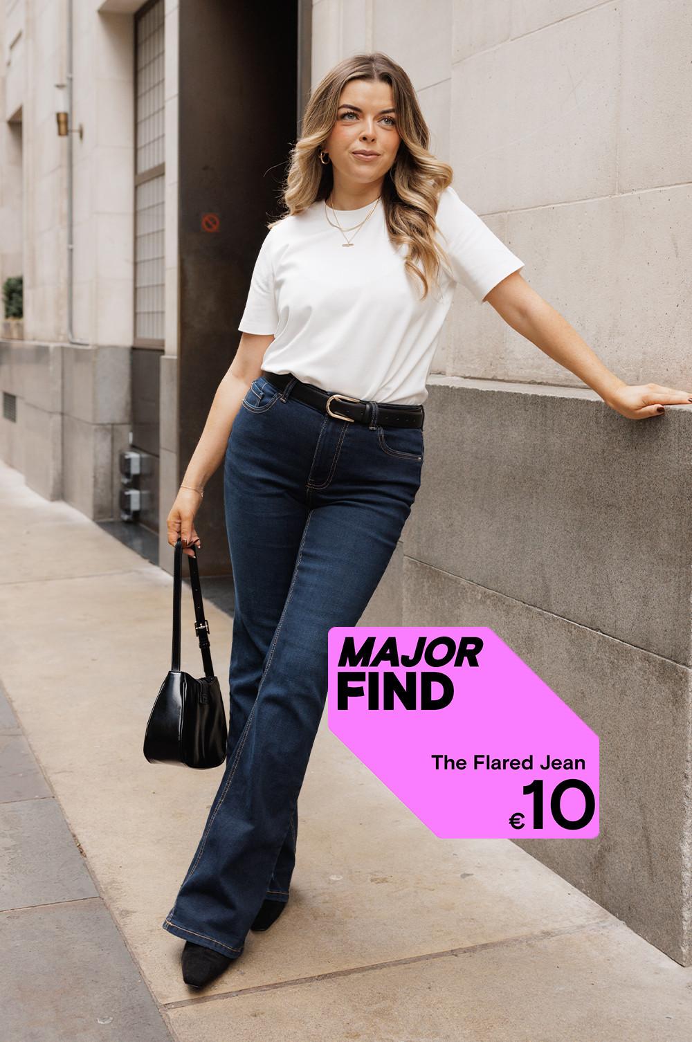 Person wearing flared jeans with white t-shirt and black handbag. Pink "MAJOR FIND" label shows €10 price