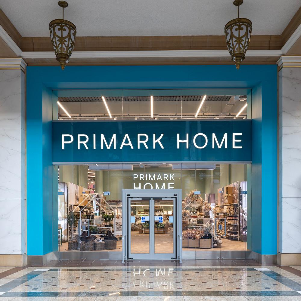 Primark Home storefront with bright blue entrance, illuminated signage and glass doors showing homeware displays inside.