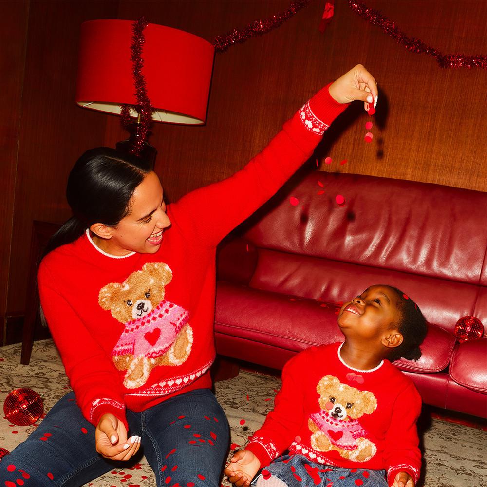 Person und Kind in passendem roten Teddybär-Weihnachtspullover mit Konfetti.