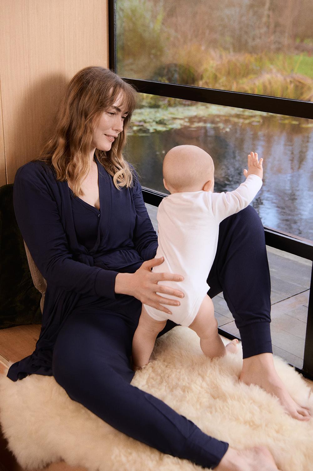 Mannequin portant un ensemble d'intérieur bleu marine, composé d'un haut à manches longues et d'un pantalon, tenant un bébé vêtu d'un body blanc à manches longues.