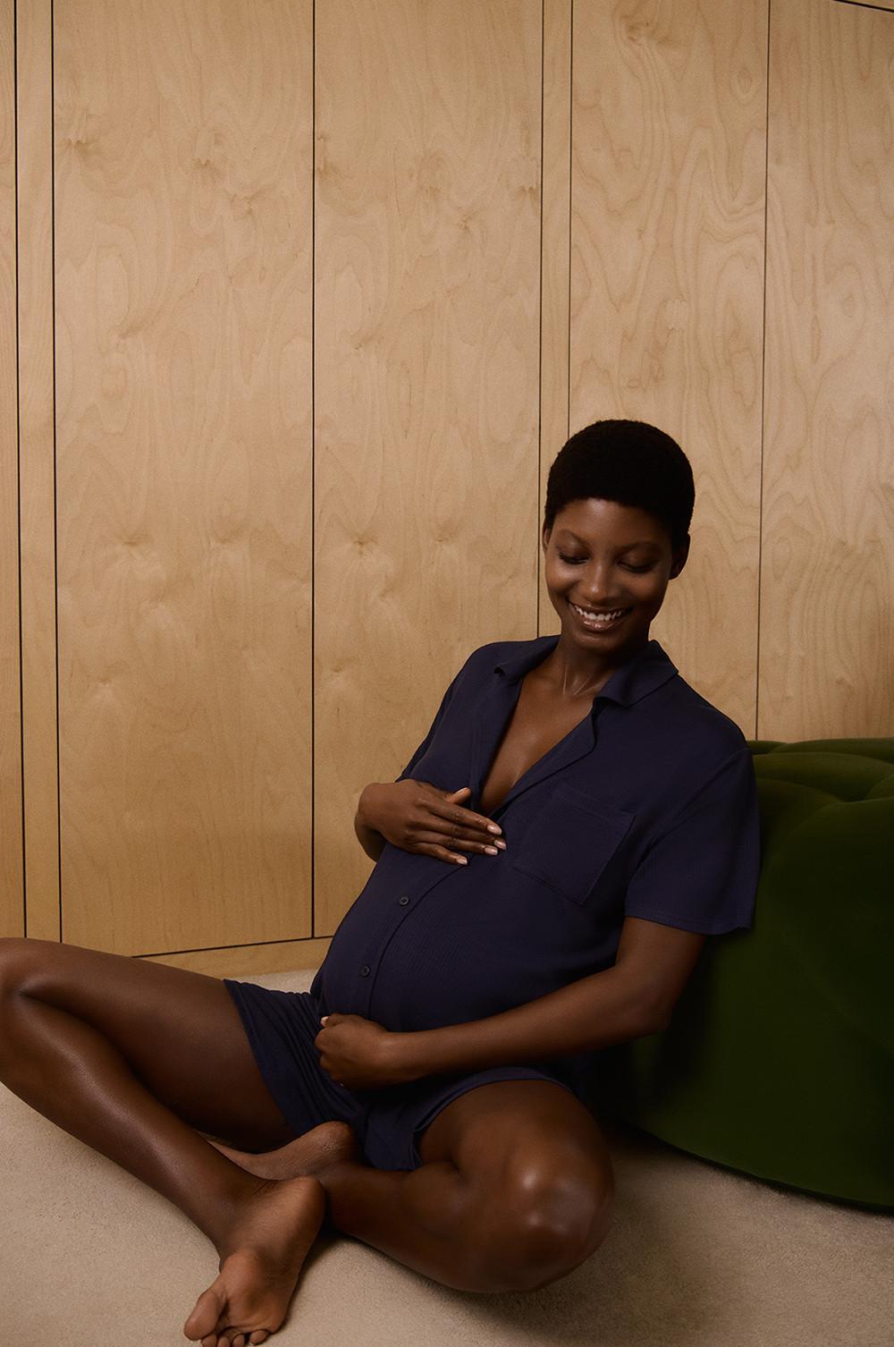 Mannequin assise sur le sol, vêtue d'une chemise de nuit boutonnée bleu marine, et tenant son ventre de femme enceinte.