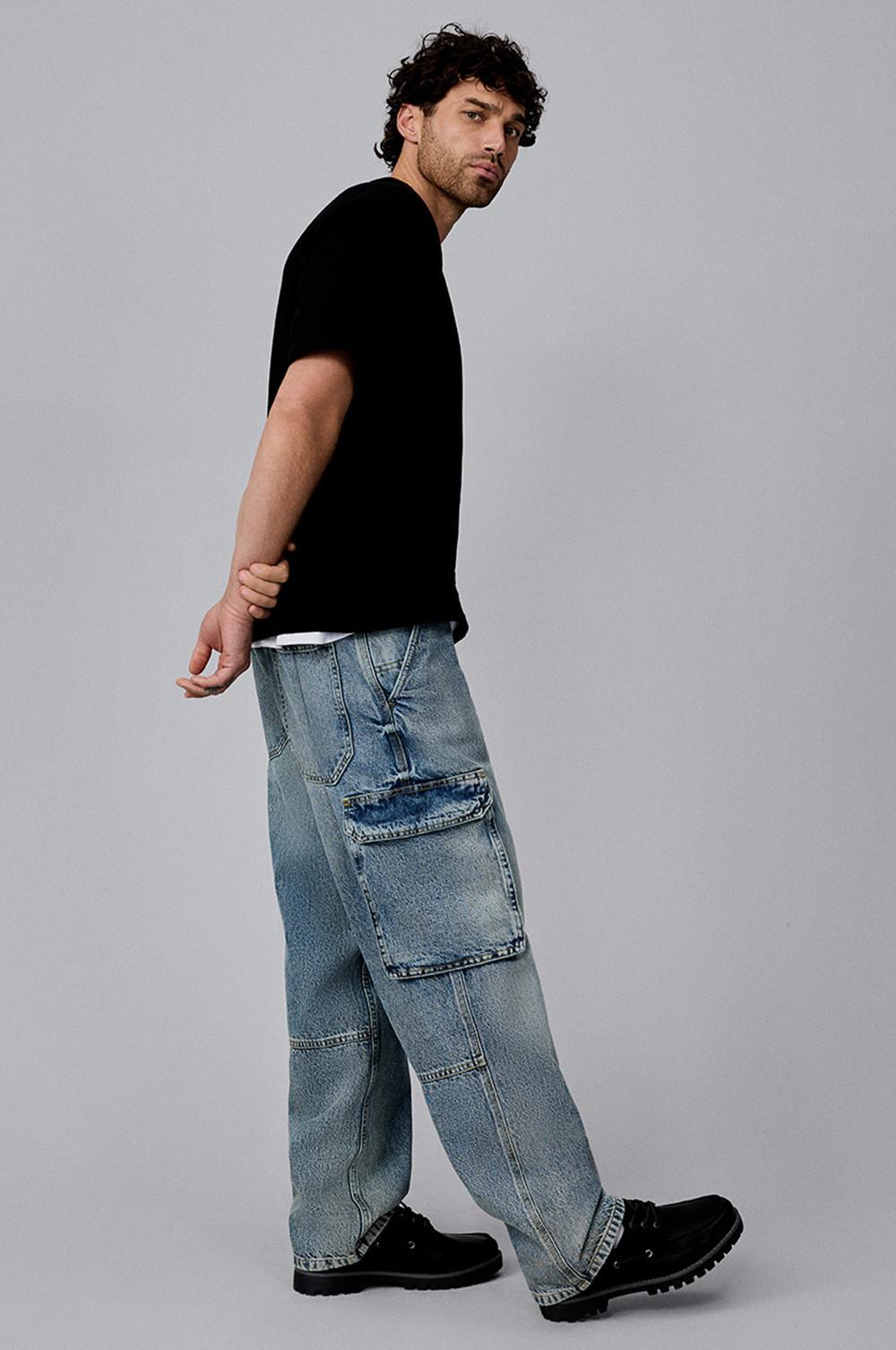 Personne de profil portant un t-shirt noir sur un jean cargo bleu clair avec des bottines noires.